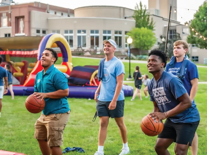 Two students shooting basketb所有s outside at an evening event.